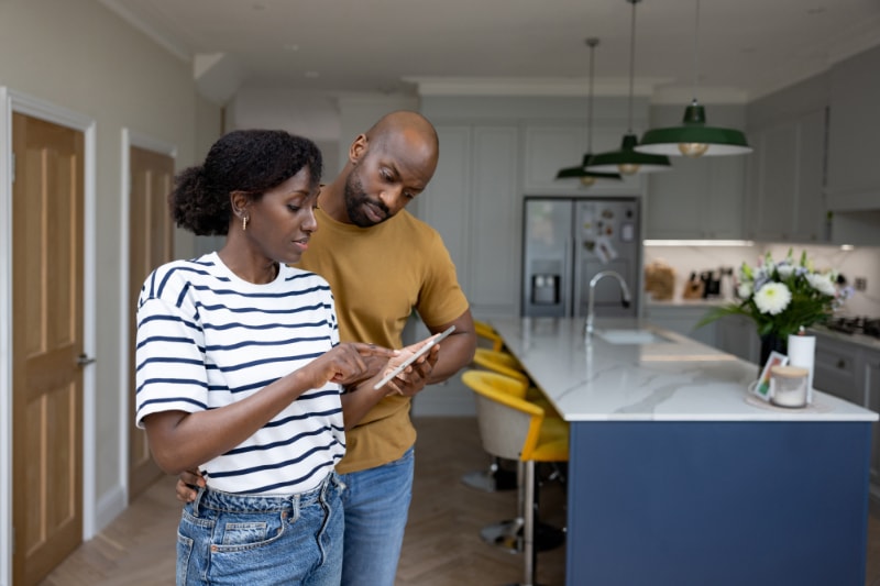 Tips to Troubleshoot Your Thermostat. African American couple controlling their smart home using a mobile app on a tablet - technology concepts.