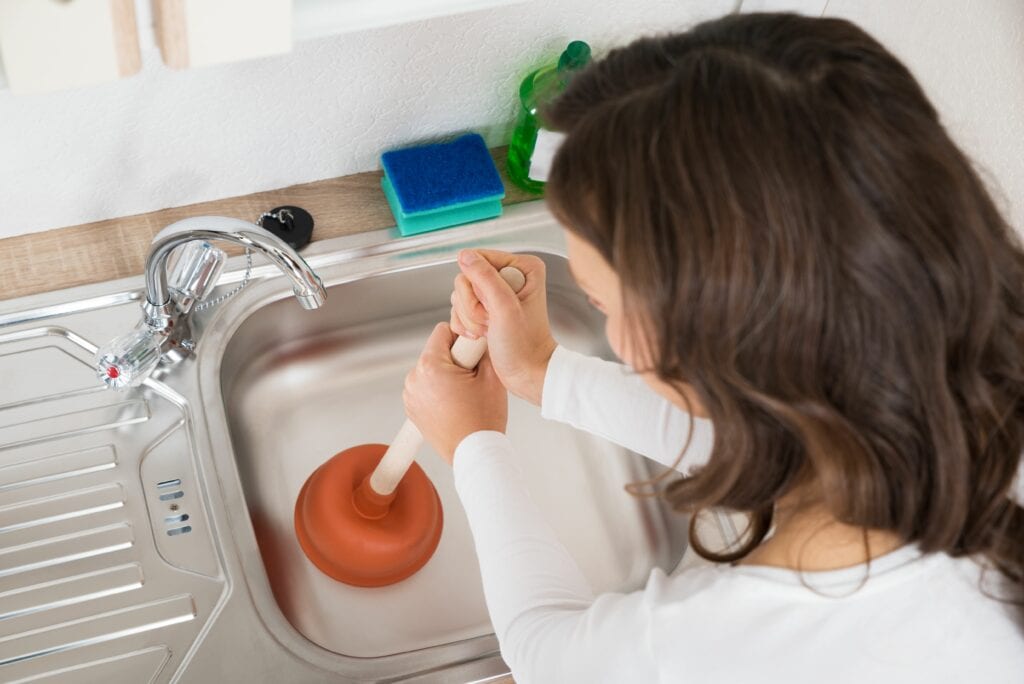 Image of someone using a plunger on their drain. Why do my drains keep clogging?