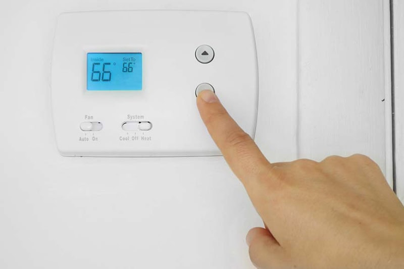 5 Reasons Why Regular HVAC Maintenance is Essential for Camden County Homeowners. Image is a photograph of a person's hand adjusting a wall mounted thermostat temperature.